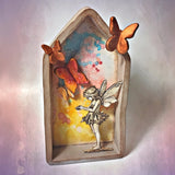 Decorative wall art with a fairy and butterflies in a decorative frame.