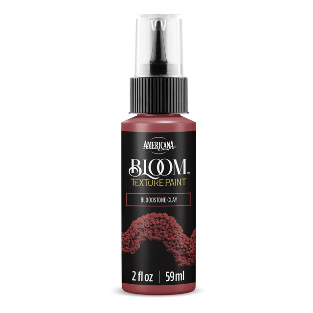 A bottle of Americana BLOOM Textured Paint in the color Bloodstone Clay, featuring a black label with red textured paint splatter graphics and a clear spray cap.