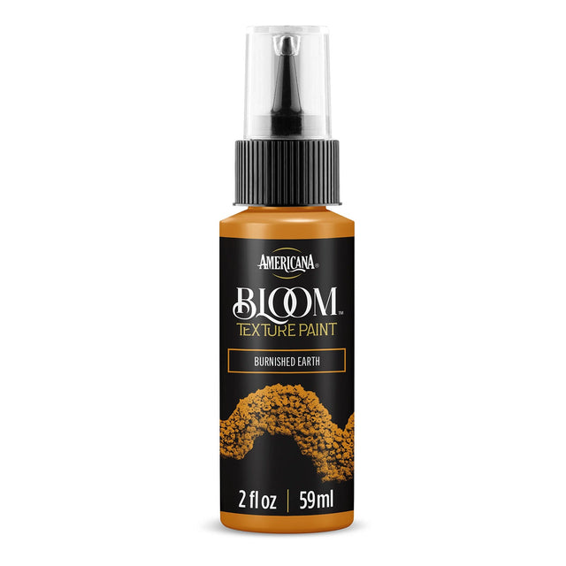 A bottle of Americana BLOOM Textured Paint in the color 'Burnished Earth', featuring a black label with gold and white text and a textured paint design, on a solid white background.