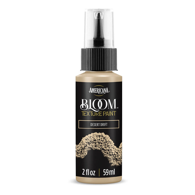 A bottle of Americana BLOOM Textured Paint in the 'Desert Drift' color, featuring a black label with gold and white lettering and a textured paint sample graphic, on a clean white background.
