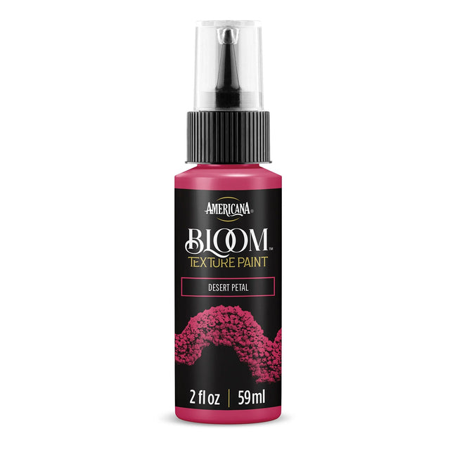 A bottle of Americana BLOOM Textured Paint in the shade Desert Petal, featuring a black label with pink and gold text and a textured pink paint design, on a white background.