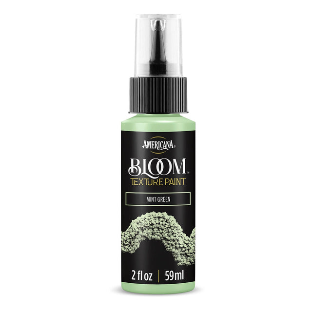 A bottle of Americana BLOOM Textured Paint in the shade Mint Green, featuring a black label with gold lettering and a textured paint sample graphic, on a white background.