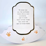 A white pet memorial plaque with a scalloped base and a central label containing a memorial quote, decorated with three orange paw print stickers.