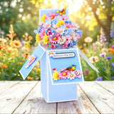 Floral-themed gift box with flowers on top, set against a natural background.
