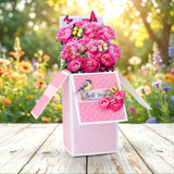 Pink gift box with flowers and decorative elements on a wooden surface with a garden background