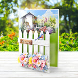 Greeting card with garden scene, flowers, and a bird on a white picket fence.
