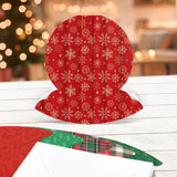 Red snowman-shaped card with white snowflakes on a wooden surface with a blurred Christmas tree background.