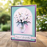 A handmade sympathy greeting card featuring white lilies in a glass vase, set against a teal and purple layered background with the text 'Deepest Sympathy' on a wooden table with a blurred garden background.