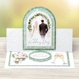 Wedding card with a couple under a floral arch, text 'On Your Wedding Day' and 'Just Married', on a wooden surface.