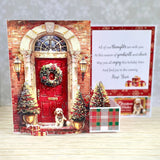 A festive New Year greeting card set displayed on a light wood surface. The main card features a detailed 3D-style illustration of a red front door with a wreath, lit lanterns, two decorated Christmas trees, and a small dog sitting at the doorstep.