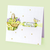 A handmade greeting card with a white embossed grid background, decorated with a 3D floral basket of yellow and purple flowers, a green and yellow 'Primrose' label, a butterfly embellishment, and small gold rhinestones, shown on a pale green background.