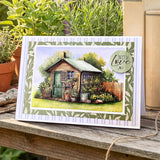 Greeting card with a garden scene and 'With Love' text, placed on a wooden surface with plants.