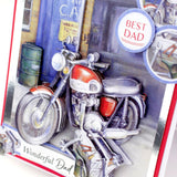 A close-up of a 3D card featuring a detailed illustration of a red and silver motorcycle parked in front of a blue garage door. The card includes layered paper elements, including a circular badge that reads 'BEST DAD' and the text 'Wonderful Dad' at the bottom.