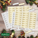 Multiple sheets of gold and white Christmas label stickers printed with 'Merry Christmas' are arranged on a rustic wood surface with holiday greenery, gold ribbons, and red berries. A KatySue logo appears in the lower left corner.