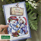 Christmas card with snowman and child design, held by a hand with greenery in the background.