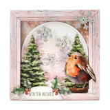 A square layered paper craft card or plaque with a distressed light pink frame. The design features a watercolor robin bird, green pine trees, silver snowflakes, holly leaves, and red berries, with the text 'WINTER WISHES' on a banner at the bottom.