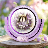 Decorative card with a wreath design featuring purple flowers and a bow, set against a blurred floral background.