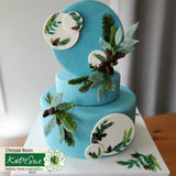 Two-tiered blue cake with floral decorations on a white surface.