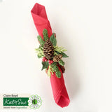 Decorative red napkin with greenery and pinecones on a white background, featuring Katy Sue Design Team logo.