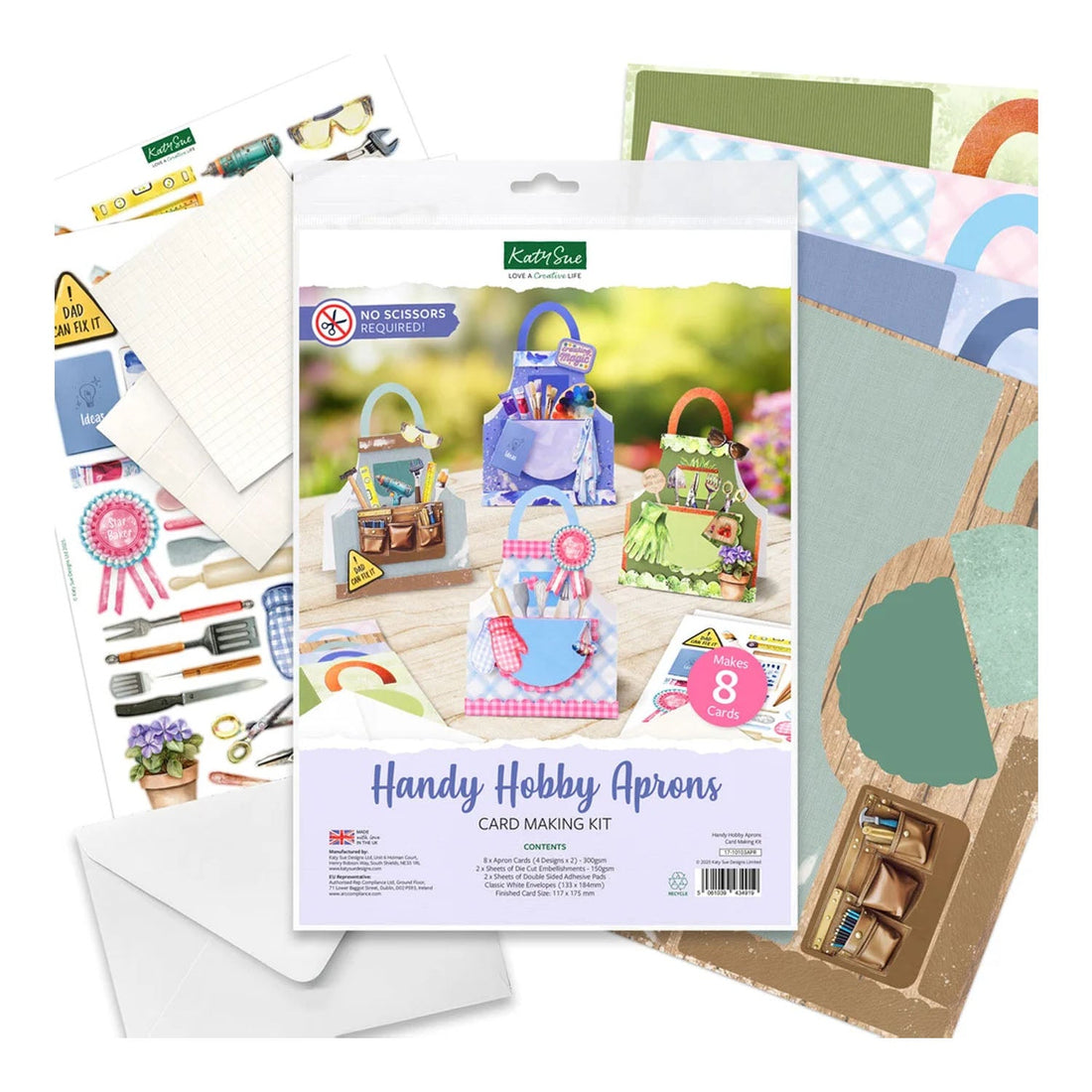 A craft kit package labeled 'Handy Hobby Aprons Card Making Kit' surrounded by included craft supplies, including patterned cardstock, envelopes, scissors, and small decorative components, arranged on a white background.