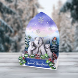 A Christmas-themed gift box or display stand featuring an illustrated winter scene with a polar bear family, snowflakes, mountains, and a robin, set on a light wood surface with a blurred snowy outdoor background.