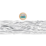 A small round wooden lid or coaster with a colorful label reading 'The Pine Tree Shop' and 'Moss Green' is shown above a long horizontal strip of gray wavy wood grain on a white background.